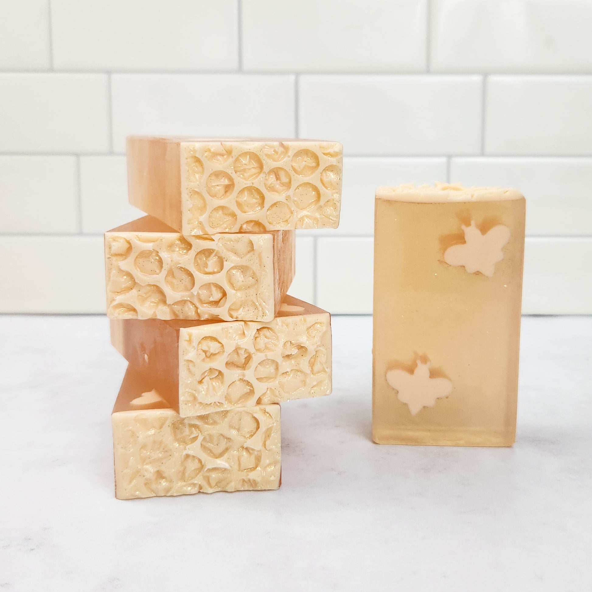 bars of honey-colored soaps featuring creamy colored bees in diagonal corners of each bar. The tops of the bars look like creamy colored honeycomb.