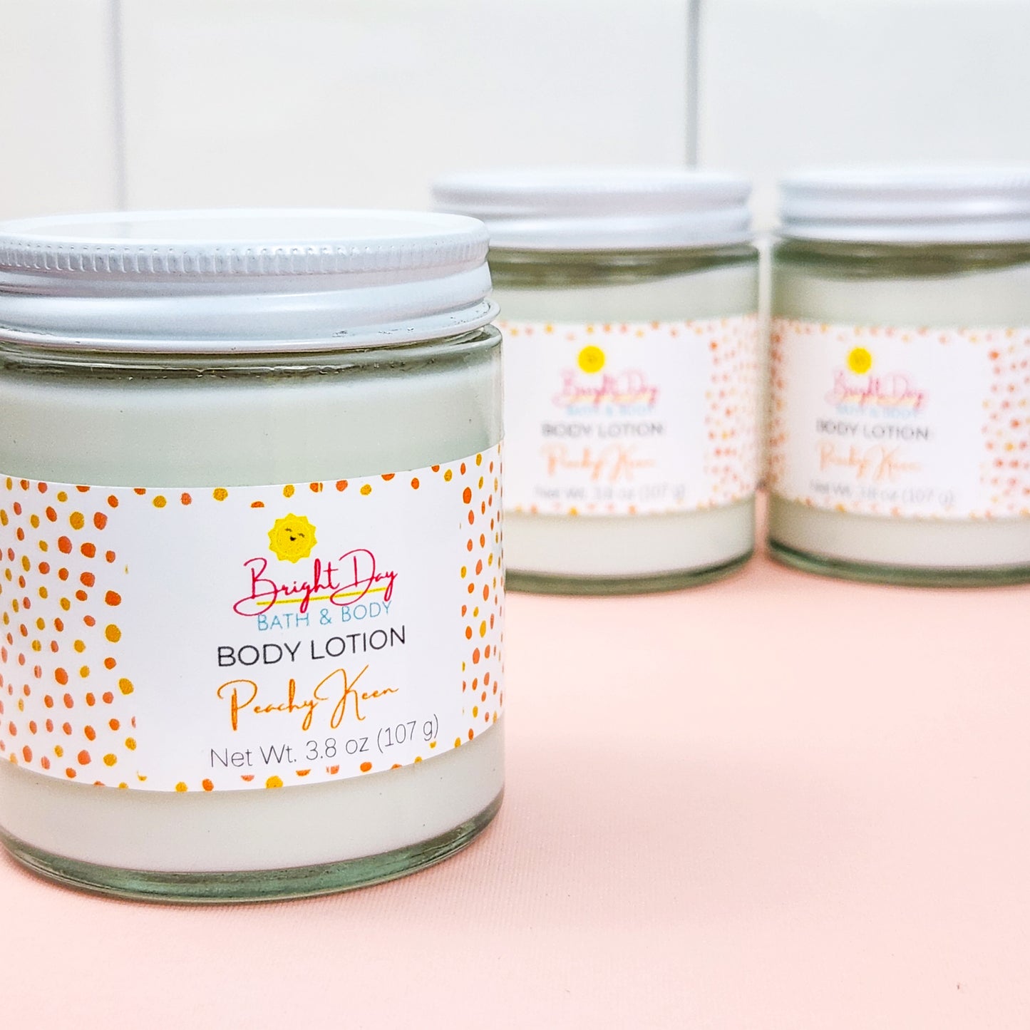 Three jars of Peachy Keen Body Lotion on a pink and white background.