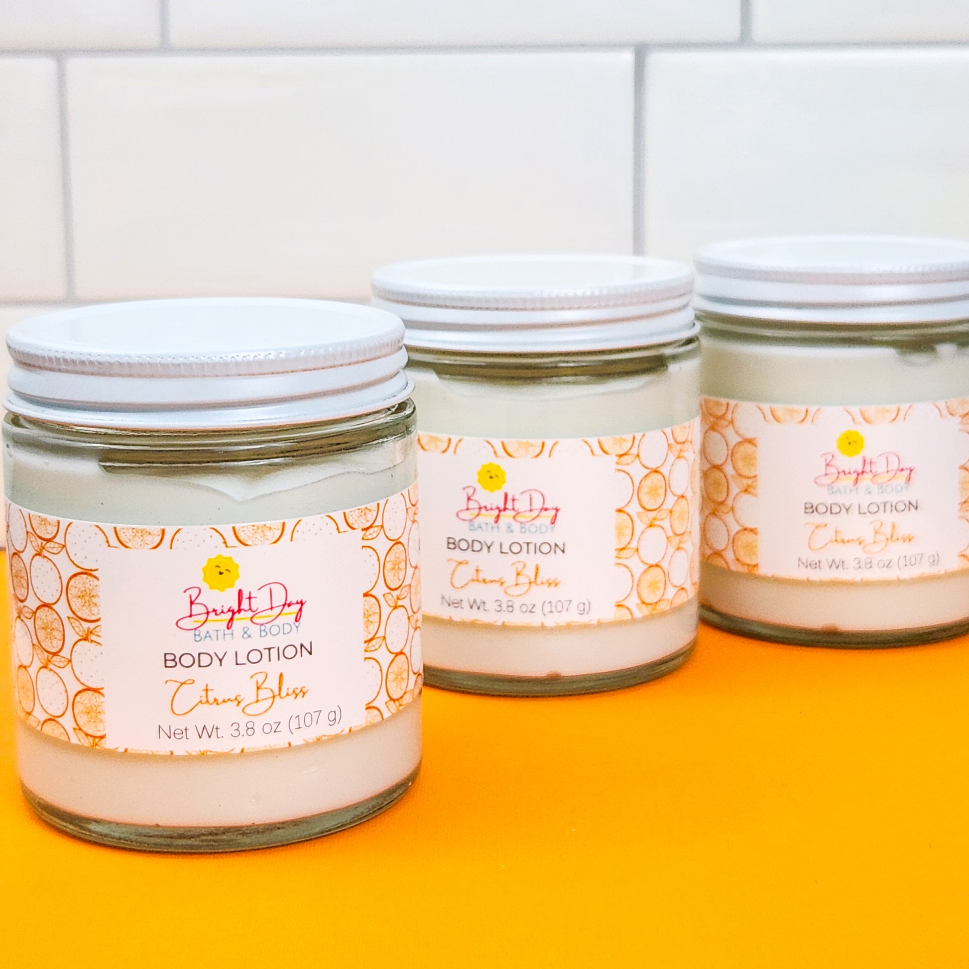 Three jars of Citrus Bliss Body Lotion on a white and orange background.