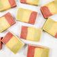 Bars of soap in a striped design of pink, yellow and green, laying on a white background.