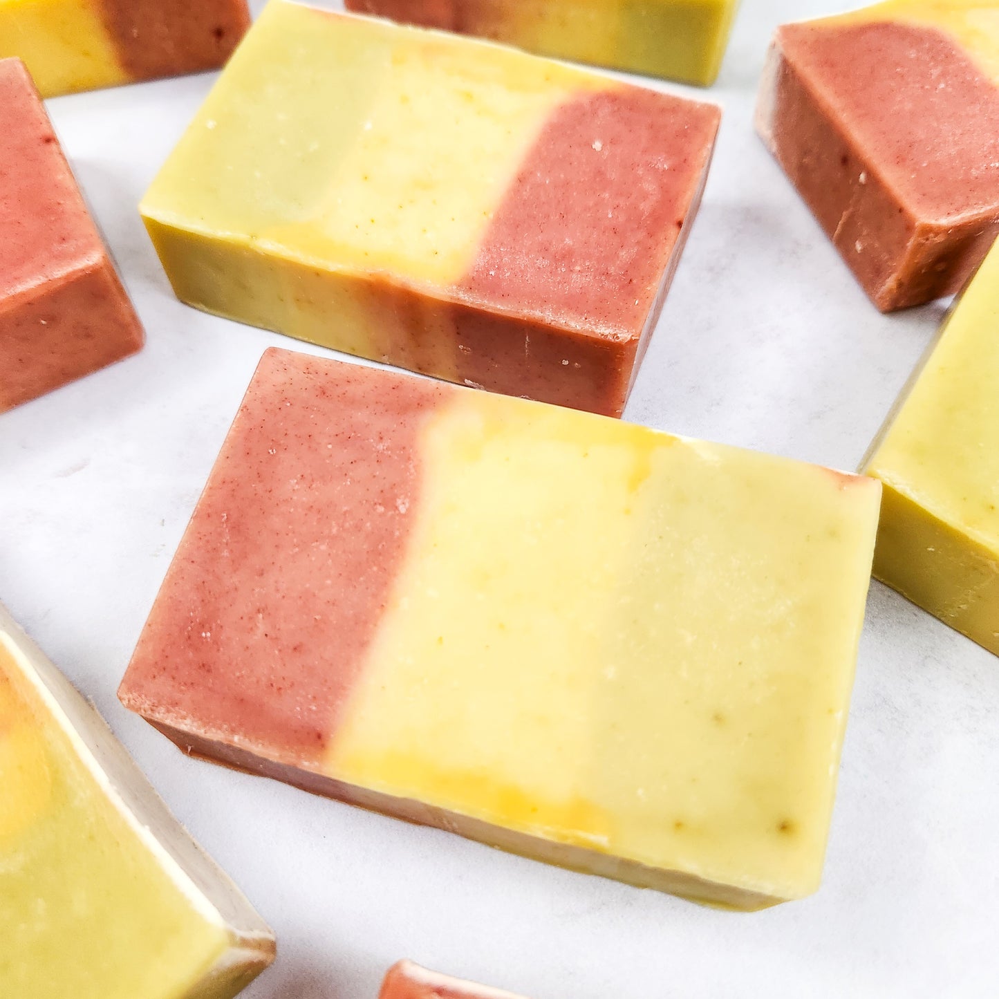 Close up of bars of soap in a striped design of pink, yellow and green, laying on a white background.