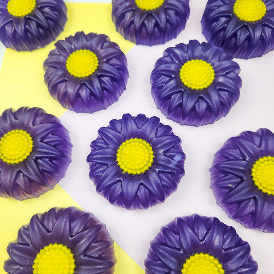 Round flower shaped soaps in purple with a yellow center. On a yellow and purple pastel background.