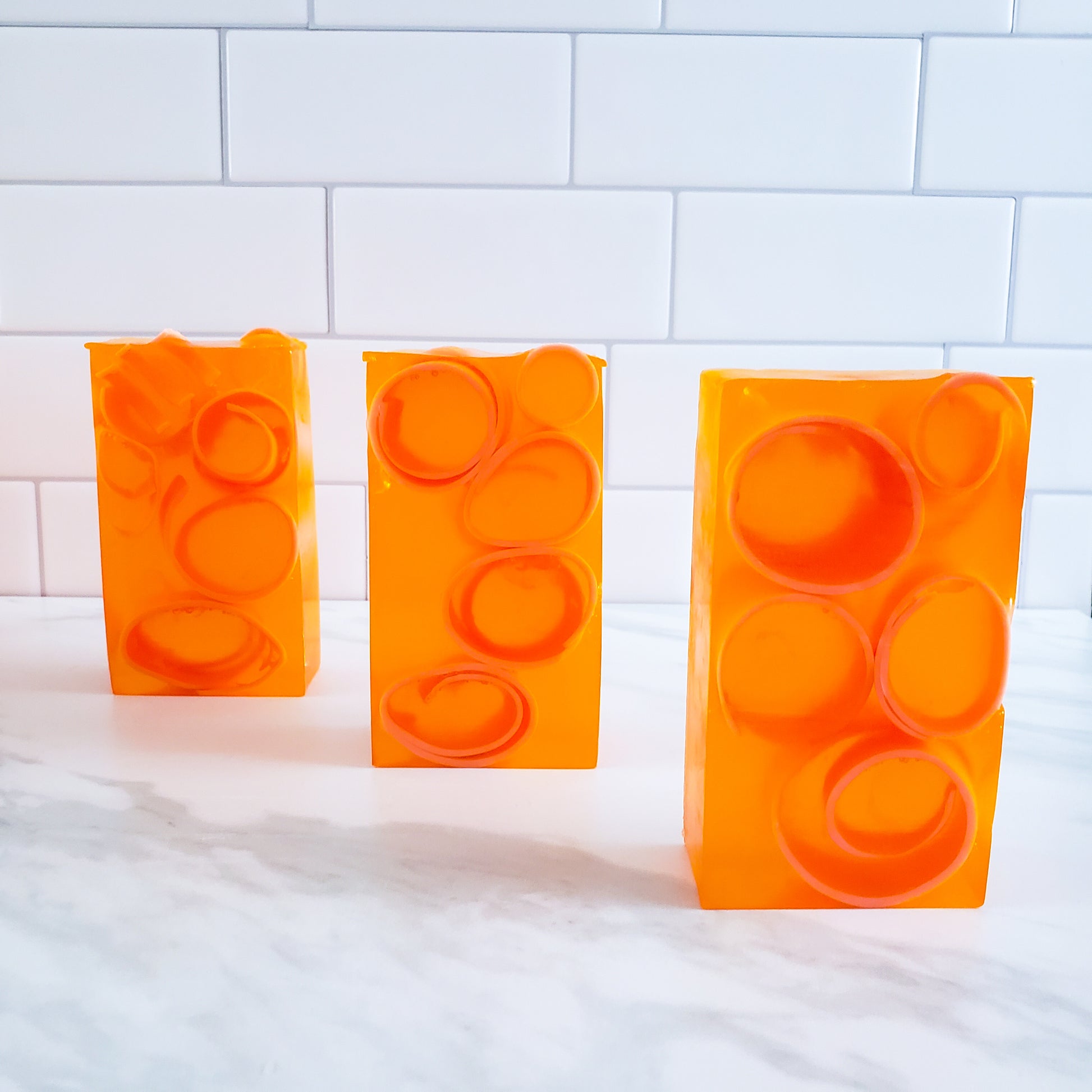 Three transparent orange bars of soap, with dark orange soap curls inside