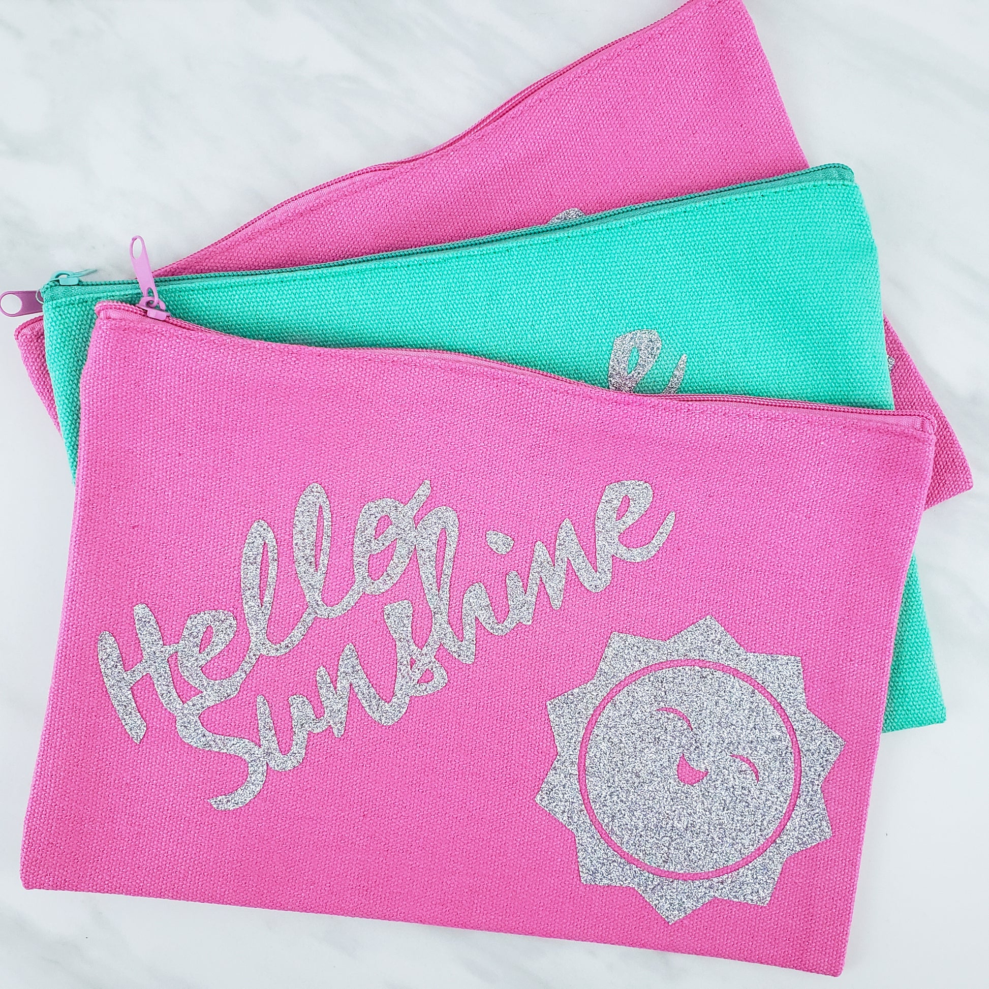 Pink and teal cosmetic bags with "hello sunshine" printed in silver