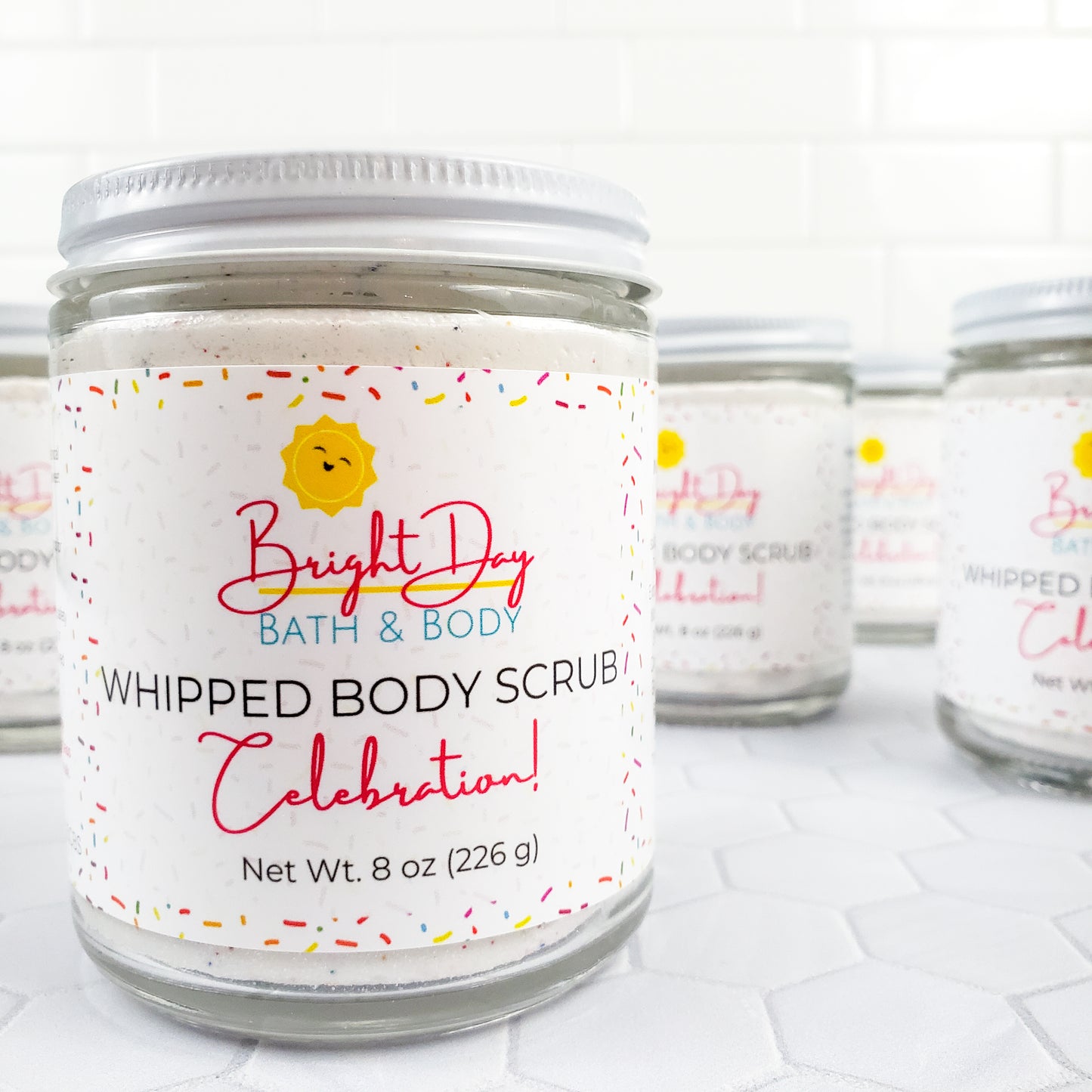 Celebration Body Scrub Jars on a tile background