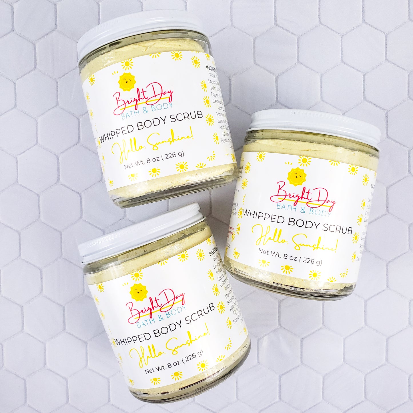 Hello Sunshine body scrub jars on a tile background