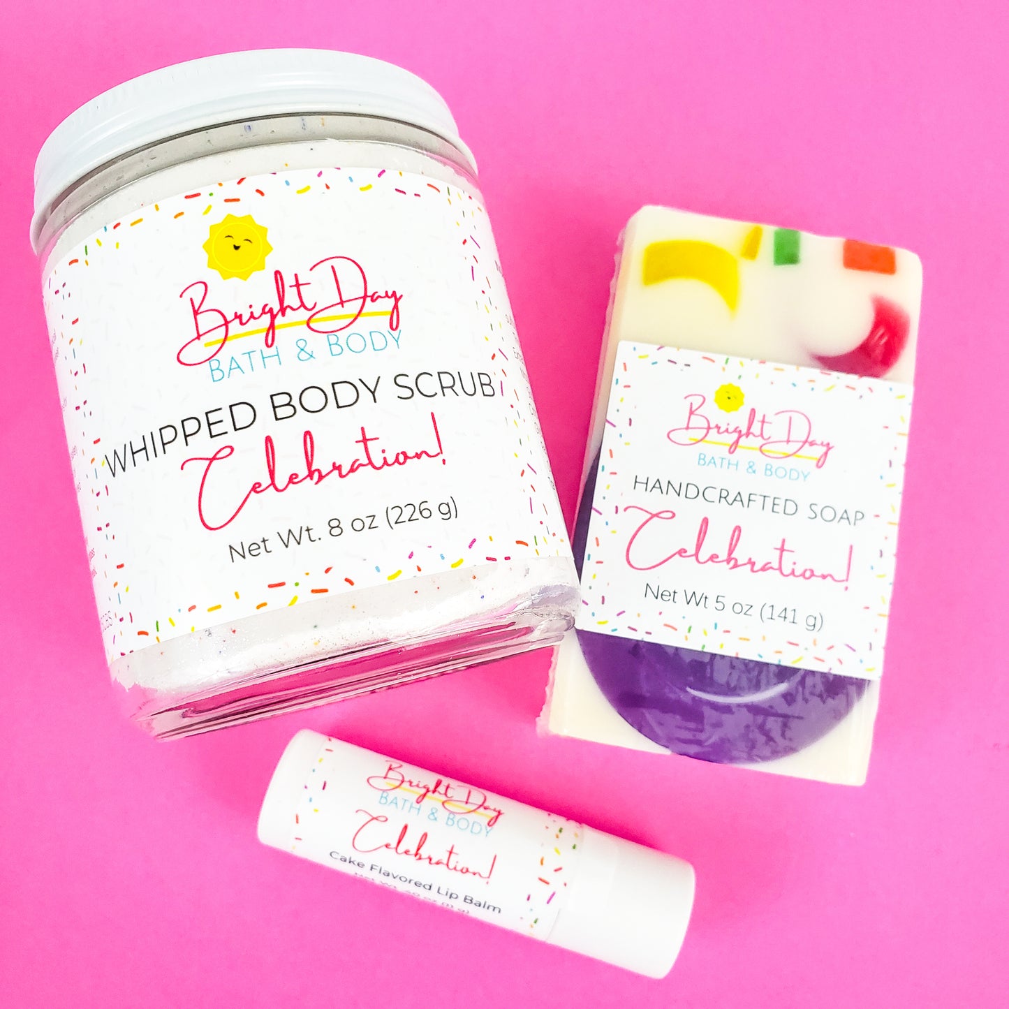 a Celebration body scrub, soap bar and lip balm on a pink background