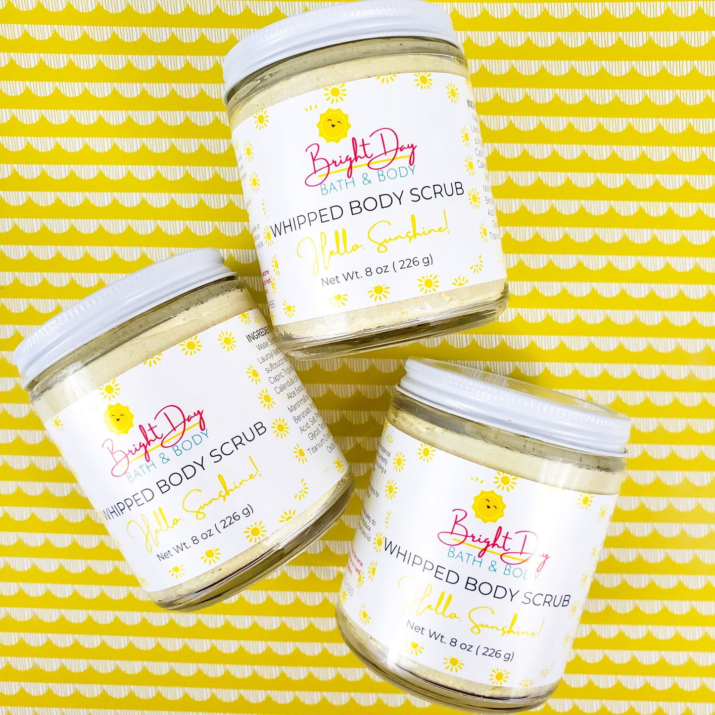 Three Hello Sunshine Body Scrubs on a yellow patterned background