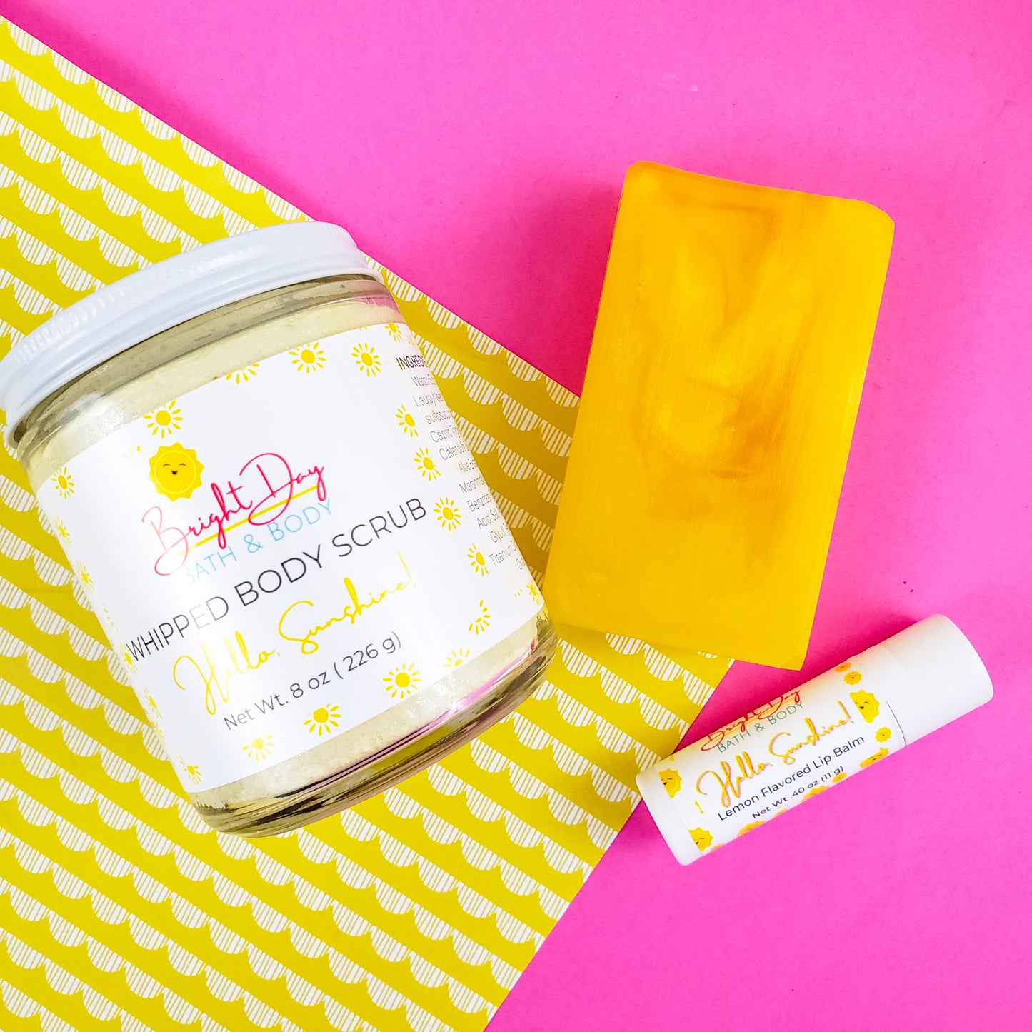 a Hello Sunshine body scrub, soap bar and lip balm on a pink and yellow background