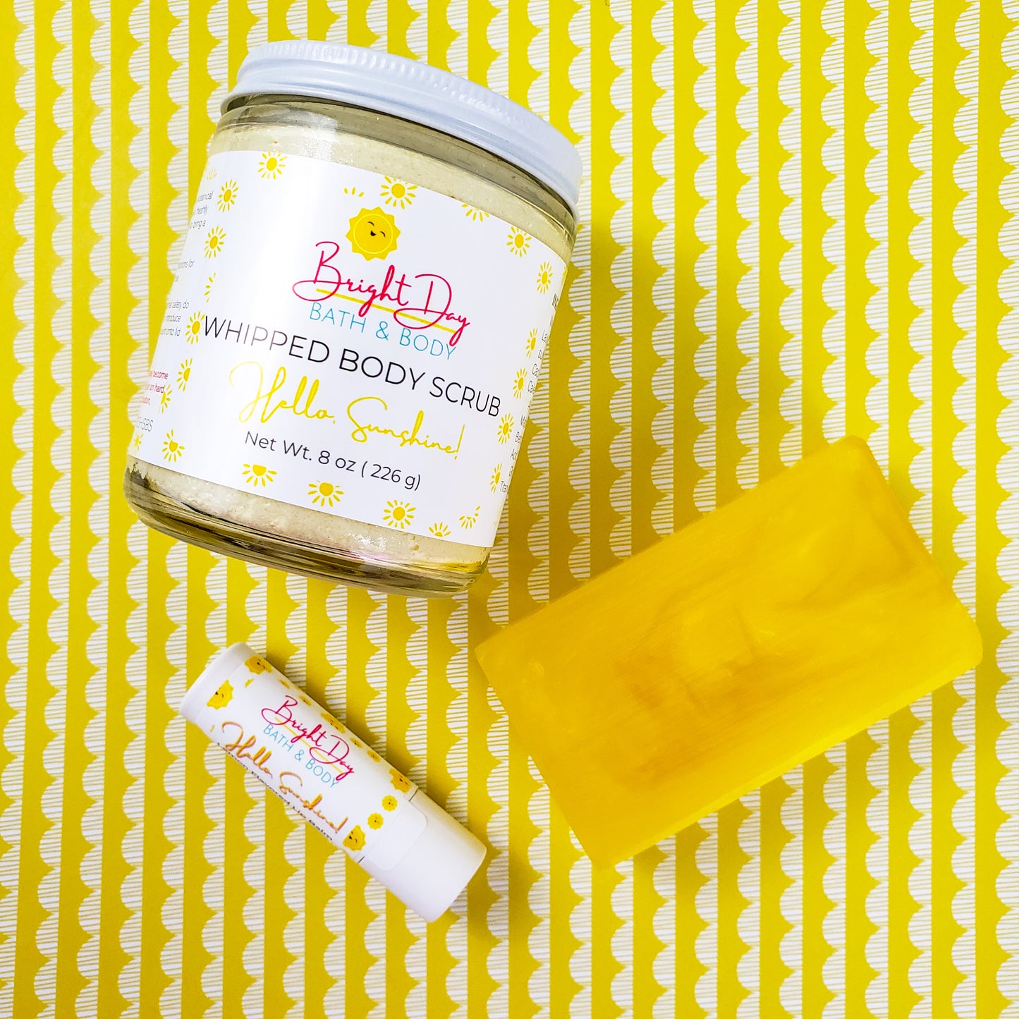 a Hello Sunshine body scrub, soap bar and lip balm on a yellow background