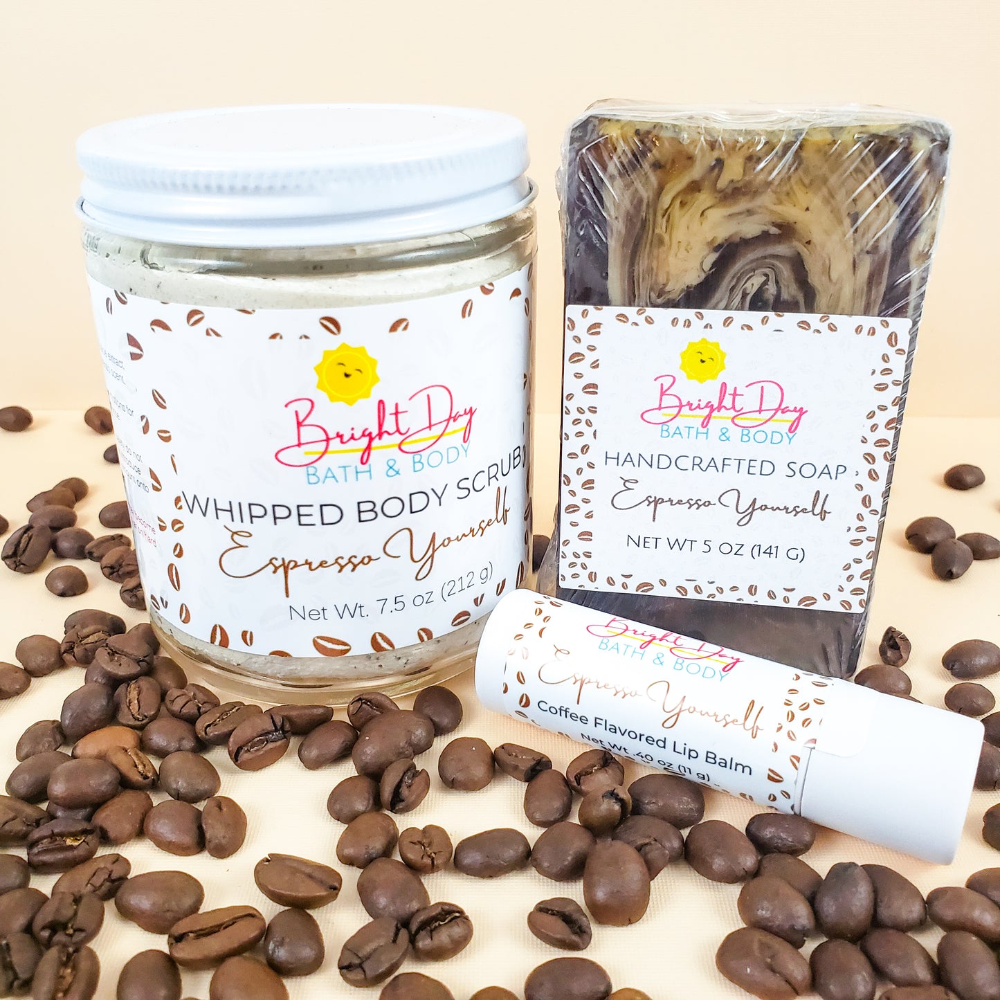 a Espresso Yourself body scrub, soap bar & lip balm on a tan background, surrounded by coffee beans