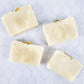 cream colored soap bars  with jasmine flowers on top on a tile background.