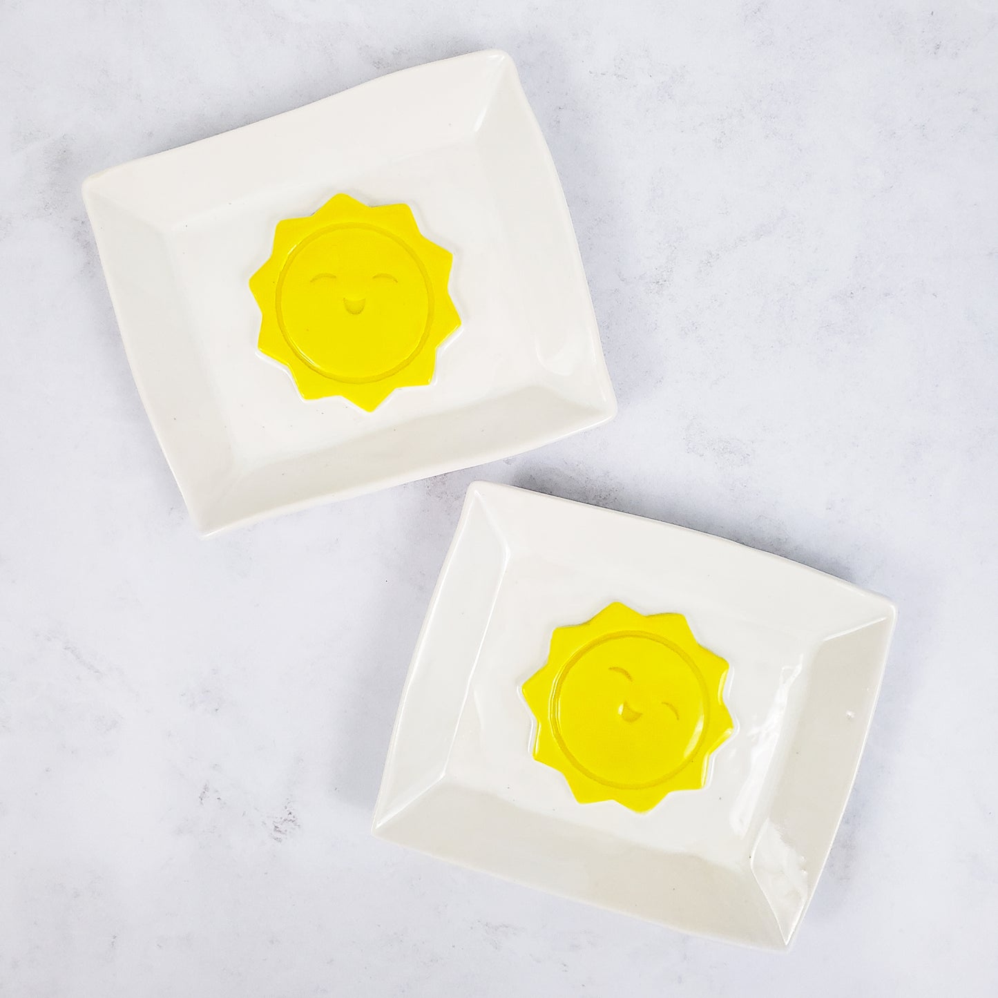 Two white rectangular soap dishes with yellow sunshines in the middle