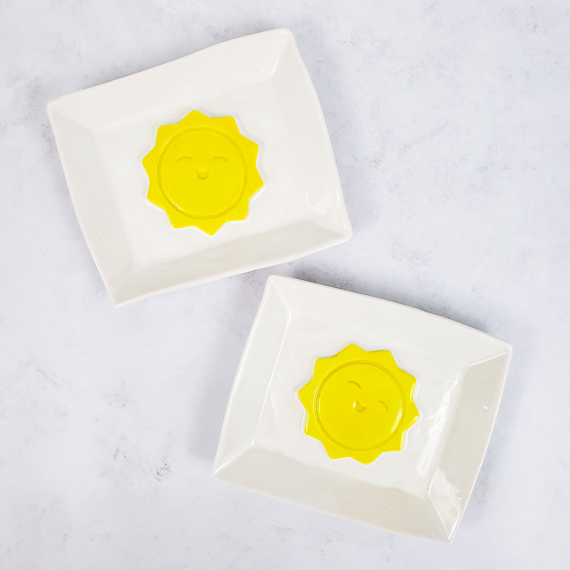 Two white rectangular soap dishes with yellow sunshines in the middle