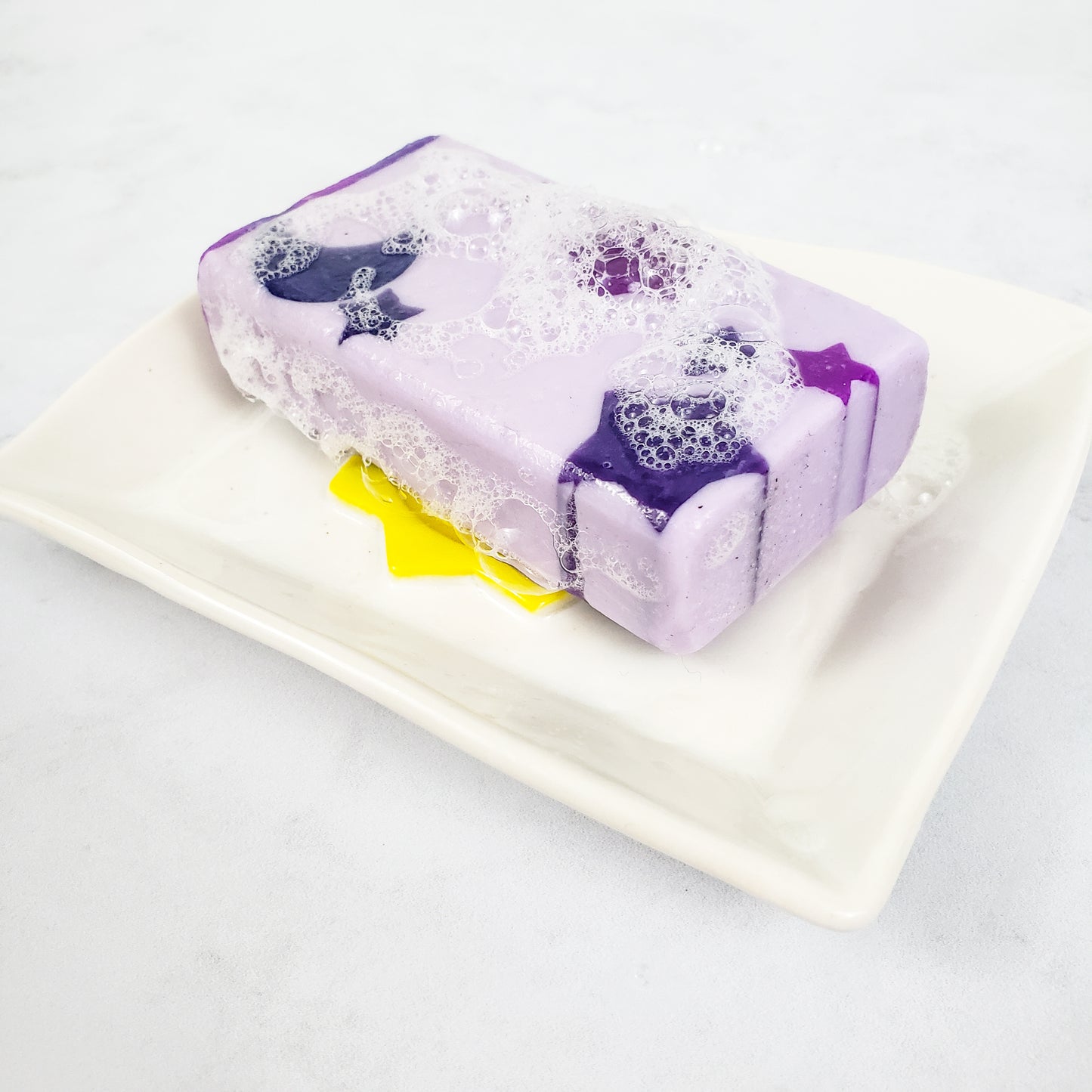 A purple soap with purple stars sitting on a white rectangular soap dish.