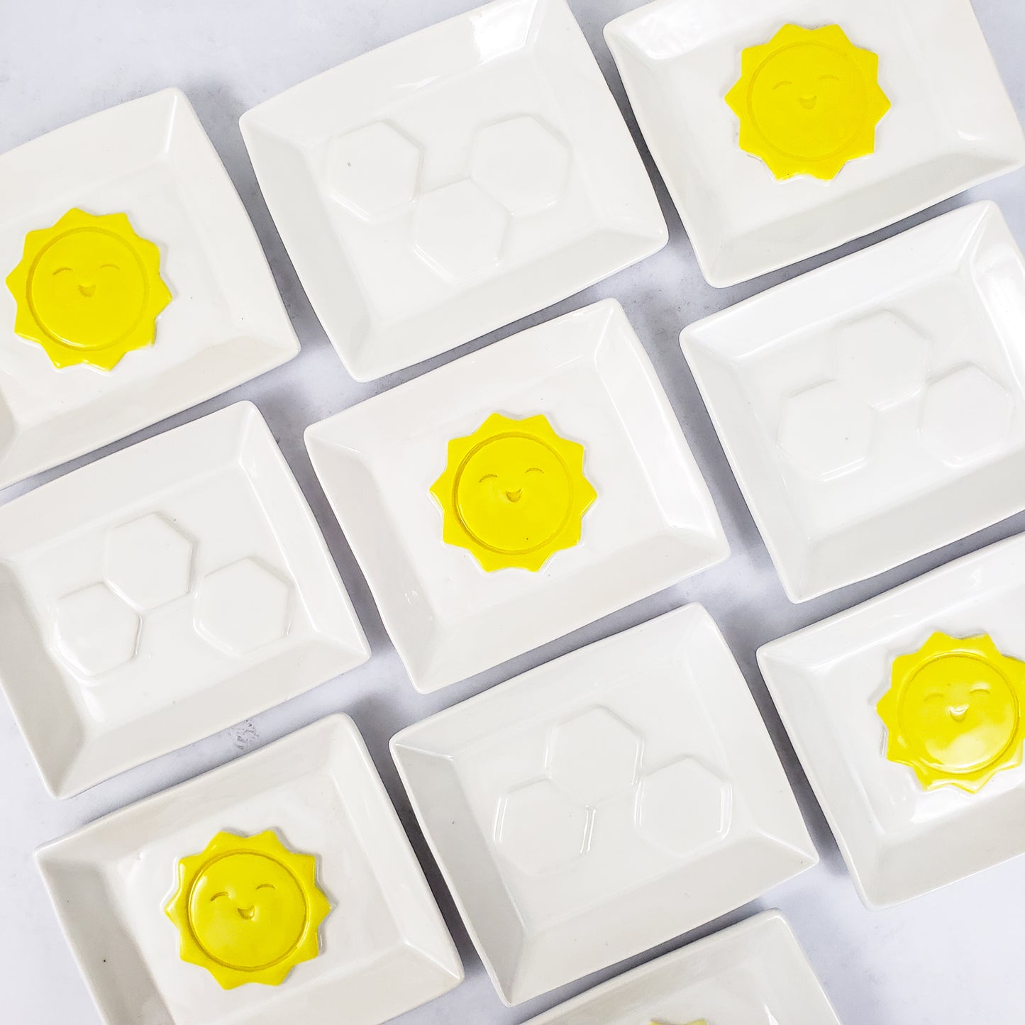 Alternating white rectangle soap dishes, some with 3 white hexagons in the middle, some with raised yellow sunshines in the middle