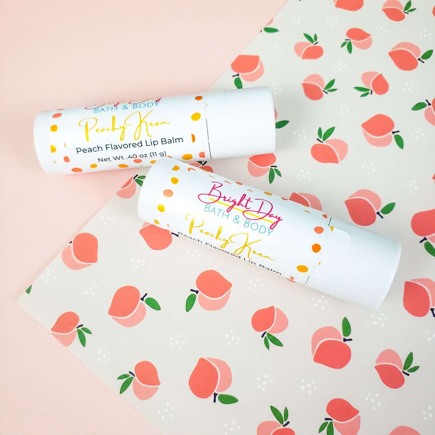 Two peachy keen lip balms on a peach decorated background