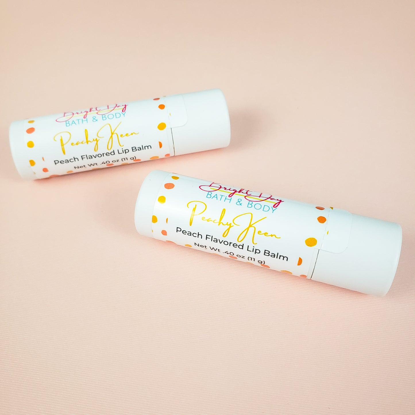 Two peachy keen lip balms on a peach colored background