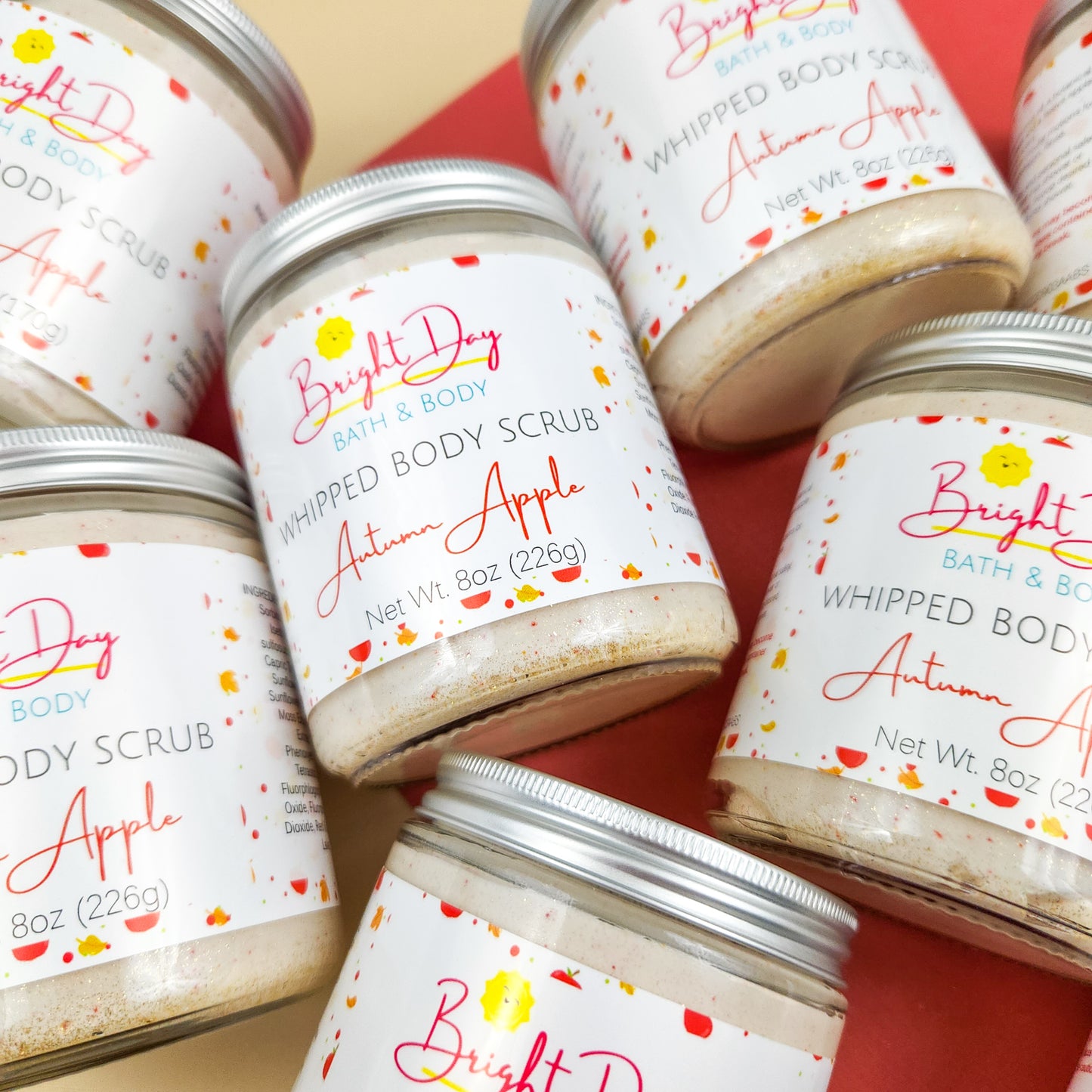 Autumn Apple Body Scrub jars on a tan & red background